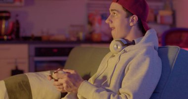 Elini keskin bir şekilde hareket ettirerek işaret işareti yapıyor. Duygusal zaferi gösteriyor. Dikkat dağıtan adam elinde bir joystickle. O video oyunu oynuyor. Kulaklıklar boynunda.. 