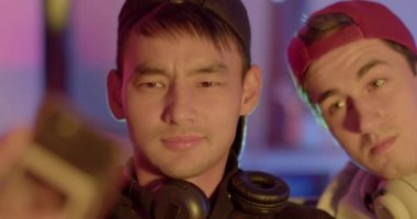 Portreciler telefonda selfie çekiyorlar. Kulaklıklar boynunda, şapkalar başında. Gadget, Bokeh 'le el ele. Yüzünde ekran ışığı var. Anılar için fotoğraf, arkadaşlarla buluşma..