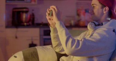 Neşeli adam bir video oyunu kazanmaktan memnun. Sonucun fotoğrafını telefonundan çekiyor. Dans hareketleri yapıyor. Kapak vizörü geri geldi. Neşe motivasyonu. CZ, Prag, Plzenska, 20.6.2022