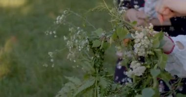 Yakın plan, çelenk yeşil dallar ve çiçekler yapıyor. Çiçekleri elleriyle örüyor. Güzel bir nesne. Ayin aksesuarı, halka şeklinde dokunmuş çiçek süsü..