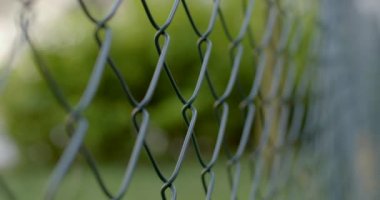 Bokeh 'deki yeşil çalıların arka planına yakın çekim. Bölgeyi geçitten korumak, hareketi kısıtlamak, sınırı işaretlemek. Çitteki metal tel..