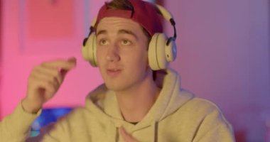 Neşeli bir adam elleri ve kafası kulaklıkla dans eder. Bir video oyunu kazanmanın keyfi. Vücutla duygularını ifade eder. Kırmızı başlıklı güneşlik..