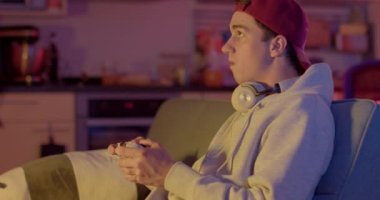 Elini keskin bir şekilde hareket ettirerek işaret işareti yapıyor. Duygusal zaferi gösteriyor. Dikkat dağıtan adam elinde bir joystickle. O video oyunu oynuyor. Kulaklıklar boynunda.. 