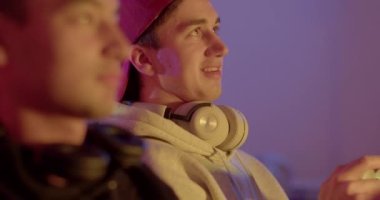 Bir arkadaşıyla konuşurken boynunda kulaklık olan bir adamın portre yüzü. Bokeh 'deki adama bakıyor. Elinde bir oyun kumandası var. Yüze hareket ışığı, aksiyon oyun odası.