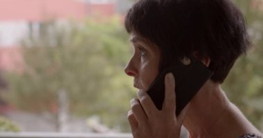 Telefonda konuşan güzel, yaşlı bir kadının yakın çekimi. Akrabalarla sohbet. Profil yüz görünümü. Yalnızlık nöbeti sırasında arama arzusu. Yaşlanma belirtisi olarak cilt kırışıklıkları.