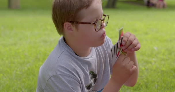 公園でカードゲームをプレイダウン症候群を持つ少年の肖像画 特別なニーズの子供の精神能力 プラハ ストロモフカ — ストック動画