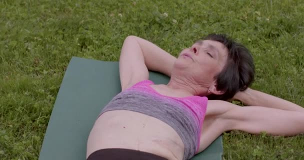 做体能训练的妇女的身体和脸部的特写 她仰卧着移动身体 增加后背的弹性 老有所事 — 图库视频影像