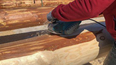 İşçi elektrikli bir aletle kütüğü öğütüyor. Bir ev inşa etme hazırlığı.