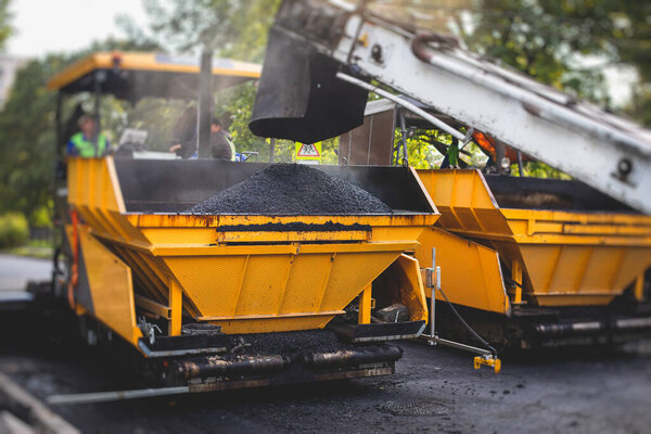 Process of asphalting, blacktopping and paving, asphalt paver machine and steam roller compactor during construction and repairing works, workers on construction site, rental vehicle workin