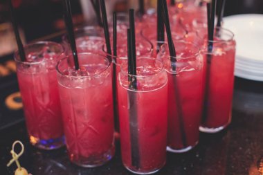 Yemek masasında alkol ayarı, bir partide sıra sıra kırmızı renkli alkol kokteylleri, martini, spritz ve dekore edilmiş yemek masasında diğerleri.