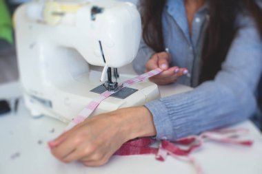 Evde elbise ve pantolonu bağlama, dikiş makinesinin kumaşlarını kapatma, kadın terzinin eliyle terzilik, terzilik, terzilik, giysi ve kumaş dikme süreci. 