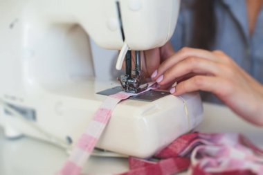Evde elbise ve pantolonu bağlama, dikiş makinesinin kumaşlarını kapatma, kadın terzinin eliyle terzilik, terzilik, terzilik, giysi ve kumaş dikme süreci. 