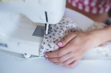 Evde elbise ve pantolonu bağlama, dikiş makinesinin kumaşlarını kapatma, kadın terzinin eliyle terzilik, terzilik, terzilik, giysi ve kumaş dikme süreci. 