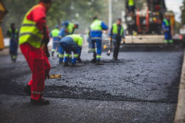 Asfalt işleme, asfalt kaplama ve asfalt kaldırım, arka planda asfalt kaldırım makinesi ve buhar silindirli sıkıştırma aracı ile asfalt tabakasını bitiren bir grup işçi.