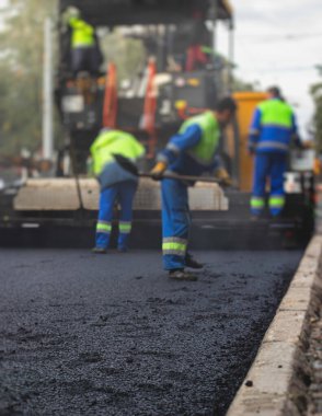 Asfalt işleme, asfalt kaplama ve asfalt kaldırım, arka planda asfalt kaldırım makinesi ve buhar silindirli sıkıştırma aracı ile asfalt tabakasını bitiren bir grup işçi.
