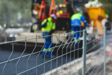 Asfalt işleme, asfalt kaplama ve asfalt kaldırım, arka planda asfalt kaldırım makinesi ve buhar silindirli sıkıştırma aracı ile asfalt tabakasını bitiren bir grup işçi.