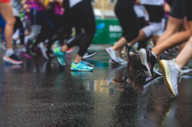 Yağmurda yarışan maraton koşucuları, şehrin asfalt sokaklarında yarı maraton boyunca koşan ayakkabı manzarası, hareket halindeki koşucular, açık hava eğitimi...