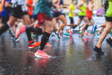 Yağmurda yarışan maraton koşucuları, şehrin asfalt sokaklarında yarı maraton boyunca koşan ayakkabı manzarası, hareket halindeki koşucular, açık hava eğitimi...