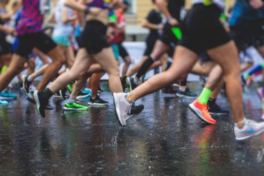 Yağmurda yarışan maraton koşucuları, şehrin asfalt sokaklarında yarı maraton boyunca koşan ayakkabı manzarası, hareket halindeki koşucular, açık hava eğitimi...