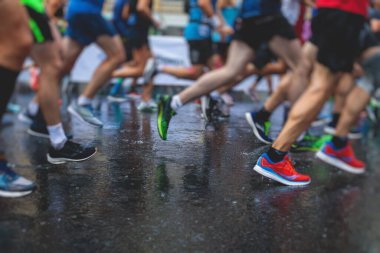 Yağmurda yarışan maraton koşucuları, şehrin asfalt sokaklarında yarı maraton boyunca koşan ayakkabı manzarası, hareket halindeki koşucular, açık hava eğitimi...