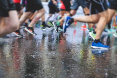 Yağmurda yarışan maraton koşucuları, şehrin asfalt sokaklarında yarı maraton boyunca koşan ayakkabı manzarası, hareket halindeki koşucular, açık hava eğitimi...