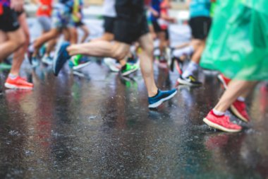 Yağmurda yarışan maraton koşucuları, şehrin asfalt sokaklarında yarı maraton boyunca koşan ayakkabı manzarası, hareket halindeki koşucular, açık hava eğitimi...