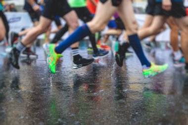 Yağmurda yarışan maraton koşucuları, şehrin asfalt sokaklarında yarı maraton boyunca koşan ayakkabı manzarası, hareket halindeki koşucular, açık hava eğitimi...