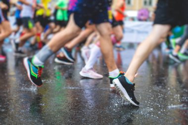 Yağmurda yarışan maraton koşucuları, şehrin asfalt sokaklarında yarı maraton boyunca koşan ayakkabı manzarası, hareket halindeki koşucular, açık hava eğitimi...