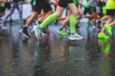 Yağmurda yarışan maraton koşucuları, şehrin asfalt sokaklarında yarı maraton boyunca koşan ayakkabı manzarası, hareket halindeki koşucular, açık hava eğitimi...