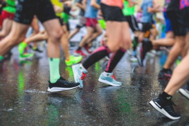 Yağmurda yarışan maraton koşucuları, şehrin asfalt sokaklarında yarı maraton boyunca koşan ayakkabı manzarası, hareket halindeki koşucular, açık hava eğitimi...