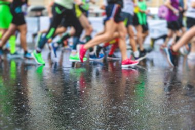Yağmurda yarışan maraton koşucuları, şehrin asfalt sokaklarında yarı maraton boyunca koşan ayakkabı manzarası, hareket halindeki koşucular, açık hava eğitimi...