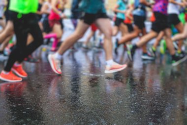 Yağmurda yarışan maraton koşucuları, şehrin asfalt sokaklarında yarı maraton boyunca koşan ayakkabı manzarası, hareket halindeki koşucular, açık hava eğitimi...