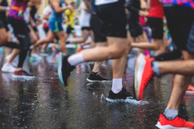 Yağmurda yarışan maraton koşucuları, şehrin asfalt sokaklarında yarı maraton boyunca koşan ayakkabı manzarası, hareket halindeki koşucular, açık hava eğitimi...