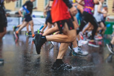 Yağmurda yarışan maraton koşucuları, şehrin asfalt sokaklarında yarı maraton boyunca koşan ayakkabı manzarası, hareket halindeki koşucular, açık hava eğitimi...