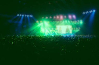 Sahne yeşil ışıklarıyla kalabalık bir konser salonu, rock gösterisi performansı, insanların silueti, bir konser festivali sırasında dans pistinde konfeti patlaması.