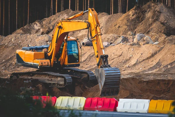 Yellow heavy excavator and bulldozer excavating sand and working during road works, unloading sand during construction of new roa