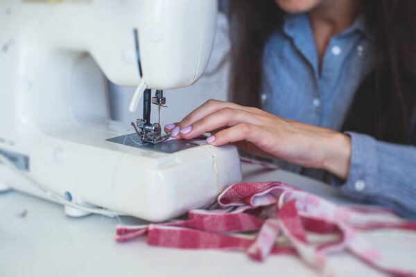 Process of hemming the dress and pants at home, close up of cloth on the sewing machine, hemming, tailoring, repairing and stitching cloth and dress, with the hand of female dressmaker 