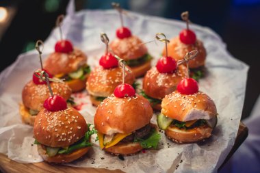 Hamburger mini burgerler ahşap bir masada kağıt üzerinde, güzel dekore edilmiş yemek masası kurumsal bir noel partisinde ya da düğün kutlamasında. 