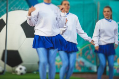 Beyaz mavi üniformalı, arka planda seyirci olan ve futbol maçında performans ve destek veren bir amigo kız grubu.