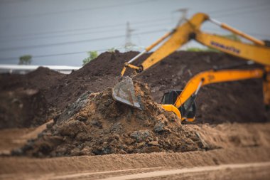 Sarı ağır kazıcı ve buldozer kumu kazıyor ve yol çalışmaları sırasında çalışıyor, yeni yol onarımı sırasında kum boşaltıyor 