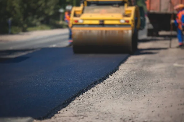 Process of asphalting and paving, asphalt paver machine and steam road roller during road construction and repairing works, workers working on the new road construction site, placing layer in summer