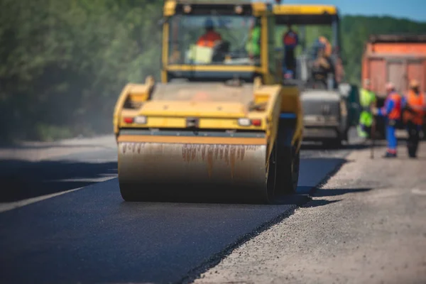 Process of asphalting and paving, asphalt paver machine and steam road roller during road construction and repairing works, workers working on the new road construction site, placing layer in summer