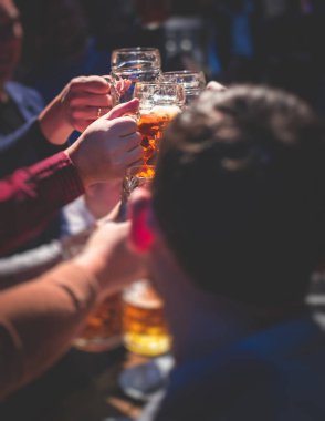 Bira festivali manzarası, bir barda altın renkli bira bardakları, filtresiz Alman buğday birası, insanların neşelenmesi ve hafif bira bardaklarıyla kadeh kaldırması, Oktoberfest manzarası