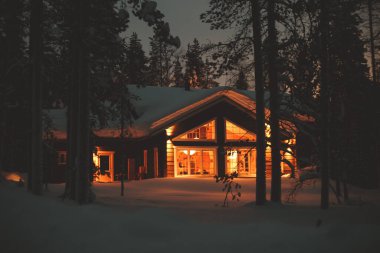 Kışın kayak merkezinin yakınındaki karla kaplı İskandinav kulübesinin sıcacık manzarası Noel ışıkları açık, akşam fotoğrafı.