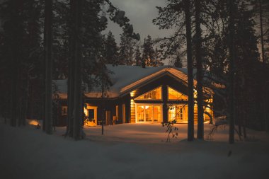 Kışın kayak merkezinin yakınındaki karla kaplı İskandinav kulübesinin sıcacık manzarası Noel ışıkları açık, akşam fotoğrafı.