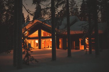 Kışın kayak merkezinin yakınındaki karla kaplı İskandinav kulübesinin sıcacık manzarası Noel ışıkları açık, akşam fotoğrafı.