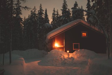 Kışın kayak merkezinin yakınındaki karla kaplı İskandinav kulübesinin sıcacık manzarası Noel ışıkları açık, akşam fotoğrafı.