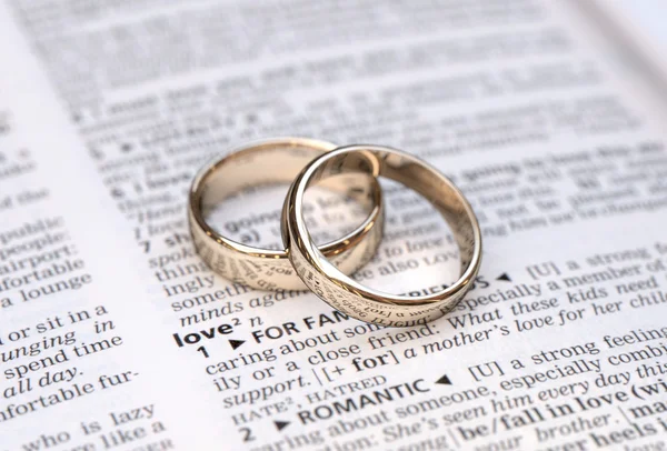 Un par de anillos de boda de oro en una página del diccionario que muestra la definición de amor — Foto de Stock