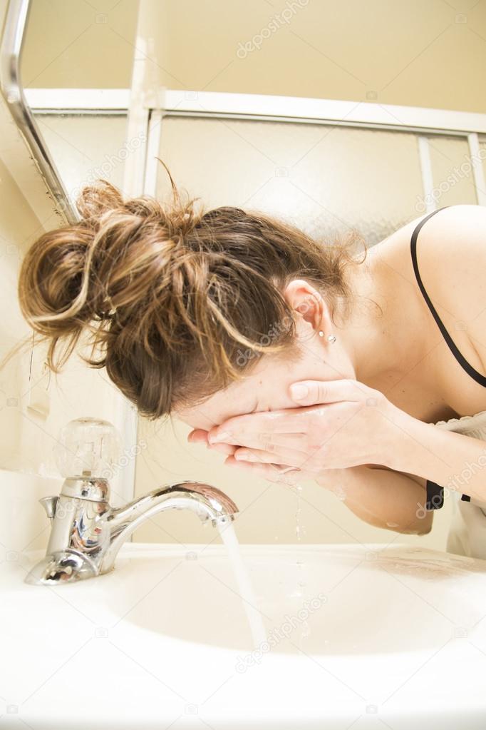 Young Woman Washing her Face in the Sink
