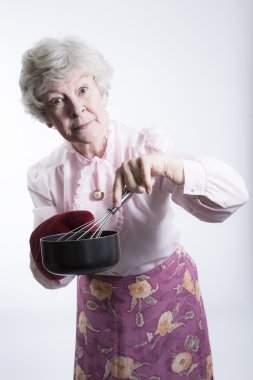 bir pot ve çırpma teli tutan yaşlı kadın